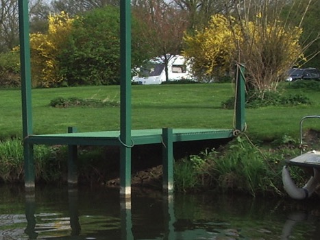 A green jetty on the riverbank in spring, with caravans beyond